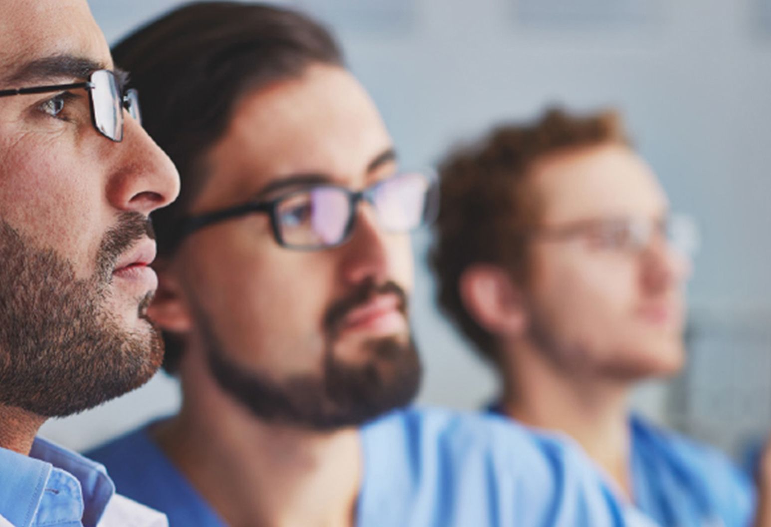 Close up of three men's faces in glasses and blue scrubs looking into the distance